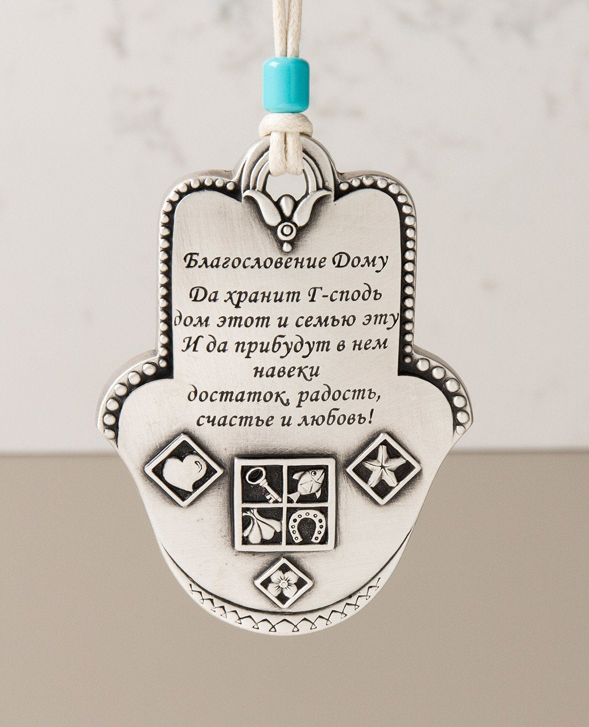 Uniquely designed sterling silver coated Hamsa Home Blessing hanging ornament. The Hamsa is decorated with embossed geometrical shapes, symbolizing abundance, fertility, success and protection from the "evil eye". The ornament makes a wonderful gift for any home, one that displays attentiveness, invoking good luck and blessings to anyone who shall receive it. Comes with a faux leather string for hanging decorated with a turquoise bead. Additional languages available: English and Hebrew. Length: 9 cm Width