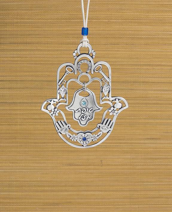 A hanging Hamsa ornament with a delicate filigree like design and a small Hamsa hanging from its center with the words "Drop of Luck". The Hamsa is decorated at its edges with pairs of motifs from the world of good luck charms and blessings, among them a pomegranate, a flower, a fish and a key. All these face each other to multiply the strength of the blessing. The ornament is coated in sterling silver and embedded with blue colored Swarovski crystals. Comes with a natural colored faux leather string, decor