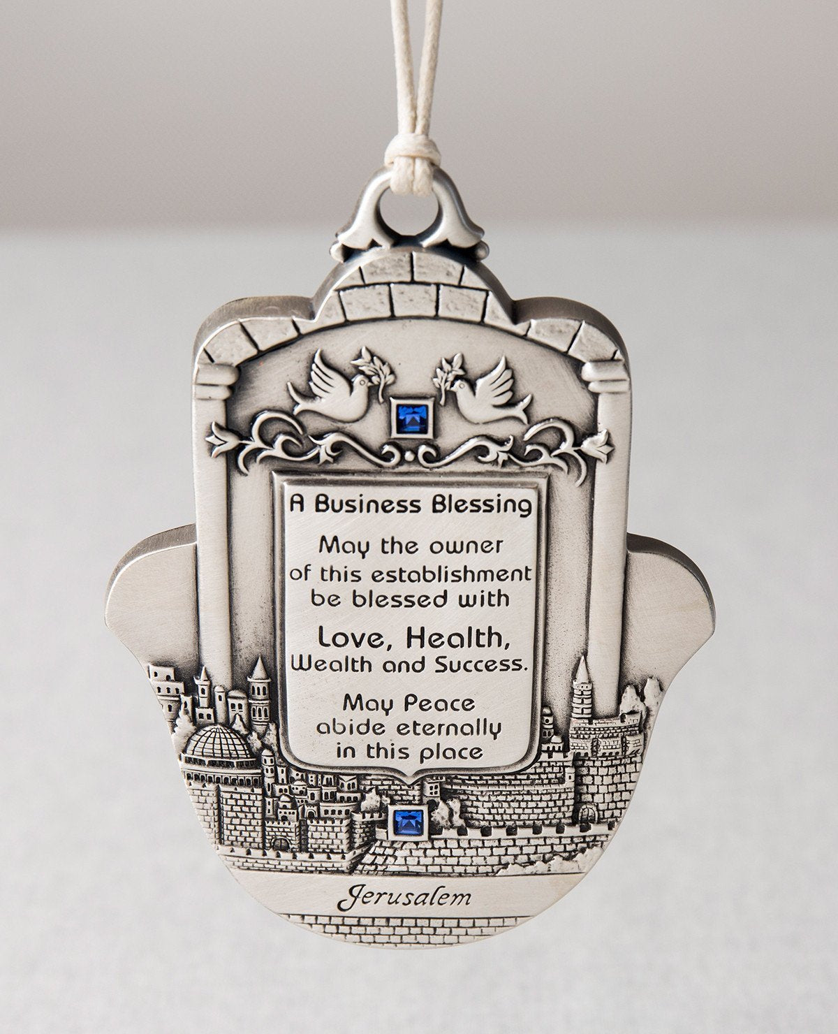 A personal and joyful blessing for any place of business which we would like to show how meaningful their work is. The greetings are embedded as a typographical engravement done by hand, with an embossed image of old Jerusalem as the background. On top are a pair of doves, symbolizing peace and tranquility. The sides are embedded with blue stones for luck and for beauty.
Sterling silver coating and a white faux leather string for tying and hanging.
Comes in language of your choice: English, Russian or Span