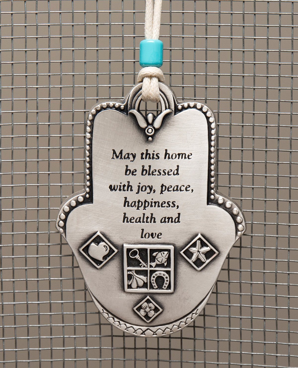 Uniquely designed sterling silver coated Hamsa Home Blessing hanging ornament. The Hamsa is decorated with embossed geometrical shapes, symbolizing abundance, fertility, success and protection from the "evil eye". The ornament makes a wonderful gift for any home, one that displays attentiveness, invoking good luck and blessings to anyone who shall receive it. Comes with a faux leather string for hanging decorated with a turquoise bead. Additional languages available: Hebrew and Russian. Length: 9 cm Width