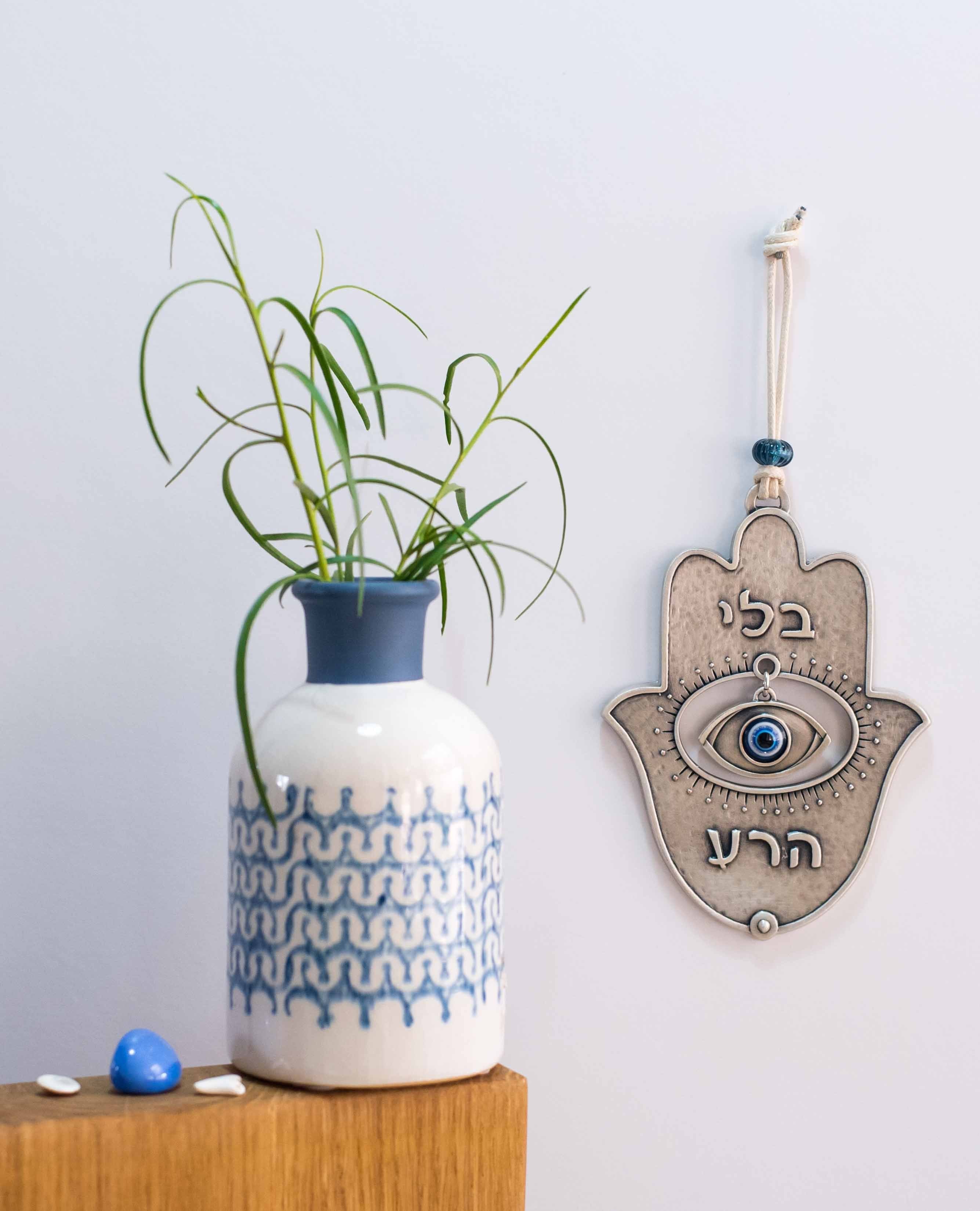 A Hamsa with a delicate and beautiful design, coated in sterling silver. At the center of the Hamsa hangs a blue eye that stands out with eyelash like decorations engraved around it to bring out its presence. Above the eye the word "No" and below it the word "Evil" are engraved - together creating the blessing and protecting sentence "no evil eye". The blue eye is considered to have qualities that fend off the evil eye, its duty for its owner is to eliminate any harm from the evil eye which is sent to us as