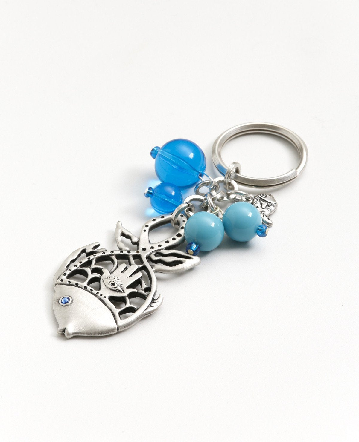 For those who like to "swim against the current" and you wish for them to "swim" safely and happily to any place they wish! A keychain with a fish element at its center, one of the symbols of abundance and luck. Artistically cut and combined with a sterling silver coated Hamsa with "drops" of turqoise beads around it resembling the sea of endless possibilities. Comes also in your choice of colorful colored stone. Length: 9 cm Width: 4 cm