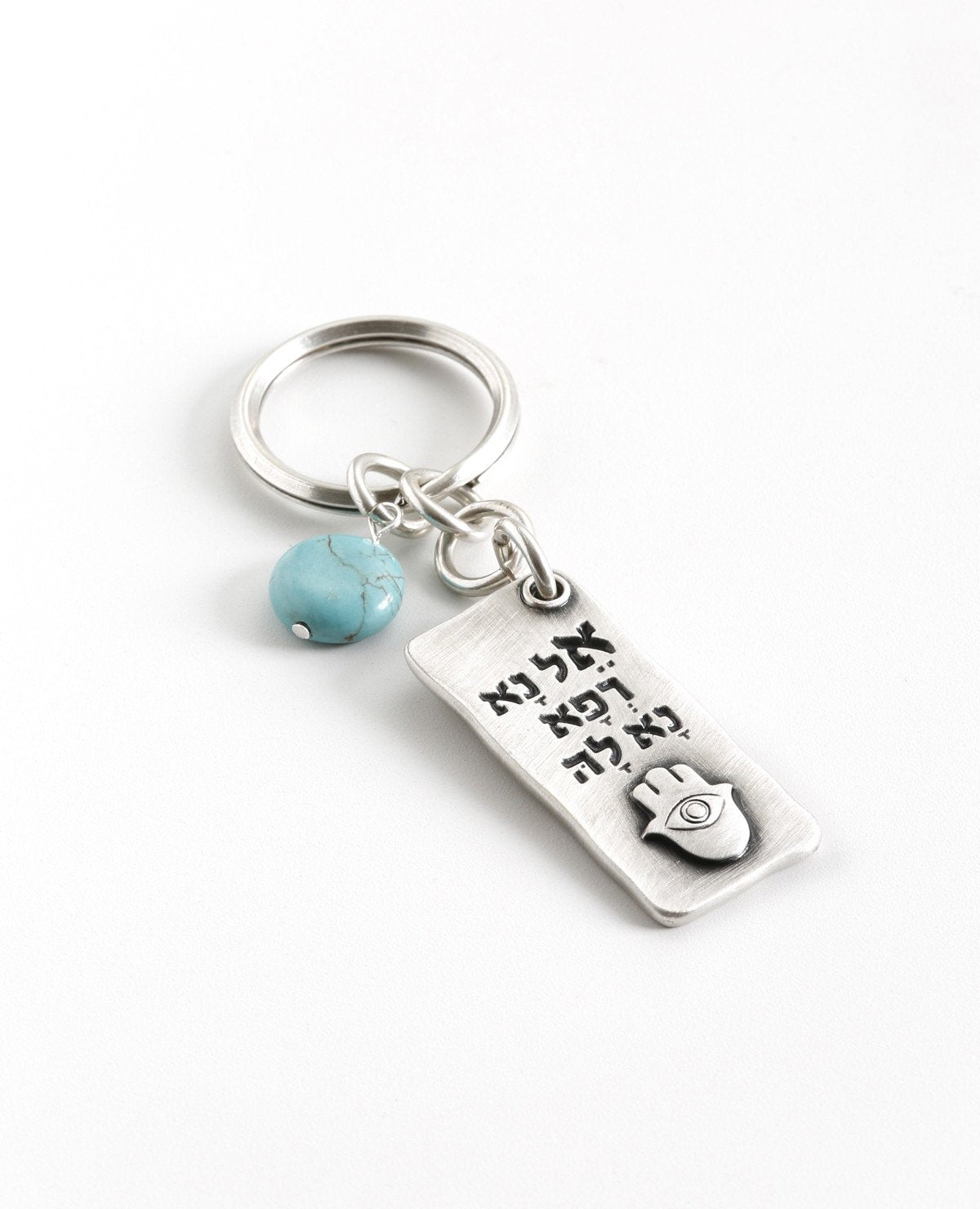 A beautiful and excitingly designed keychain, the content of which was taken from a prayer by Moses for the health of his sister, and it is in fact a prayer for good health. Shaped as a rectangular plate that has the sentence "Please, God, heal her" written in Hebrew on one side, and underneath an embossed image of a Hamsa with an eye. The other side contains blessings, in both English and Hebrew, for quick recovery, good health, and longevity. Next to the plate hangs a pretty turquoise stone. The keychain