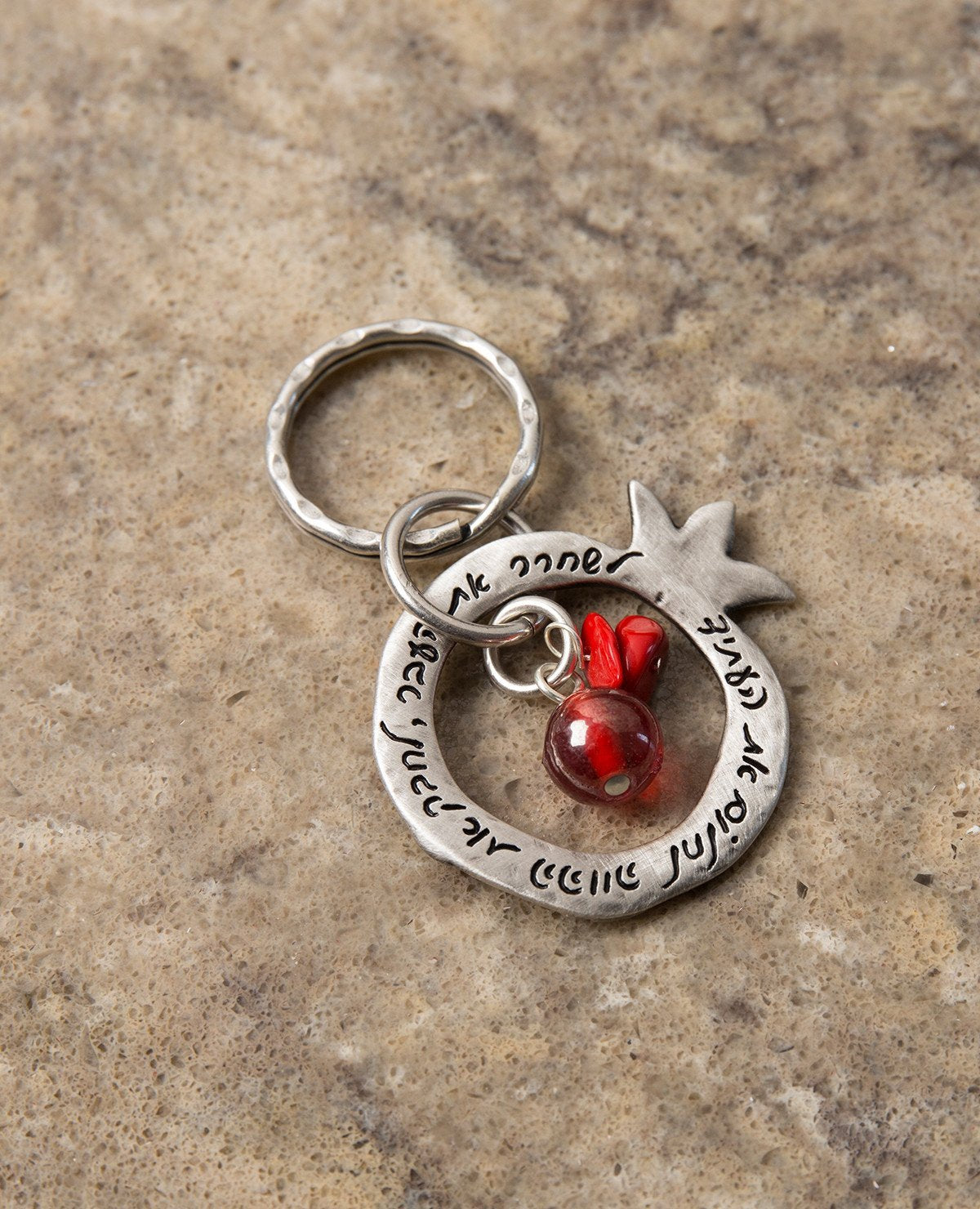 A charming keychain with an important message for life. The keychain is designed as a hollow pomegranate coated in sterling silver. At its center hang a red bead and two beautiful red stones. Written on one side of the pomegranate frame are the words "Let go of the past, embrace the present, dream the future". On the other side of the frame are little pomegranate decorations. The keychain is strong and reliable. A wonderful and exciting gift for him or for her, or for anyone in fact who wants to live life a