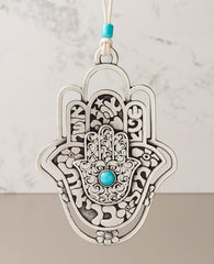 A hanging Hamsa ornament, designed in exquisite beauty: a Hamsa within a Hamsa within a Hamsa. The outer one - a hollow frame decorated by delicate flowers. The middle one - all embossed words of blessing - for abundance, luck, health, happiness and love. The inner one - filigree decoration with a turquoise stone at the center. The ornament is coated in sterling silver and comes with a faux leather string deocorated by a turquoise bead. An impressive and very meaningful gift that is a pleasure to grant to o
