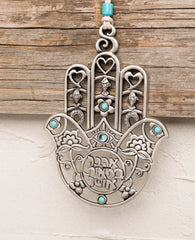 A Hamsa hanging wall ornament, gently designed and full of presence. The more you look at it the more and more you discover details and motifs that intensify its beauty. You can find motifs of a heart, a horseshoe, and a fish... Can you spot the birds? The special cut which creates a variety of different shapes, the intertwined flowers, the turquoise colored stones... in short, a medley of designs and blessings in words and symbols. A gift you will want to gaze at more and more and give again and again. The