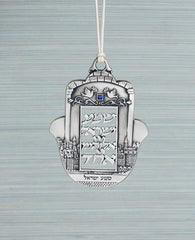 A prestigious and inspiringly designed hanging "Shema Israel" ornament. The Hamsa is coated in sterling silver and decorated at its sides by an engraved view of the walls of Jerusalem and its stones. At the center is a blank plaque with the words "Hear, O Israel, the Lord is our God, the Lord is one". Above the plaque is an engraved image of two doves with an olive branch and a blue colored Swarovski crystal embedded in between them. The ornament comes with a natural colored faux leather string for hanging.