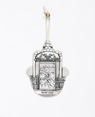 A prestigious and inspiringly designed hanging "Shema Israel" ornament. The Hamsa is coated in sterling silver and decorated at its sides by an engraved view of the walls of Jerusalem and its stones. At the center is a blank plaque with the words "Hear, O Israel, the Lord is our God, the Lord is one". Above the plaque is an engraved image of two doves with an olive branch and a blue colored Swarovski crystal embedded in between them. The ornament comes with a natural colored faux leather string for hanging.
