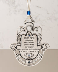 An impressive and richly designed Business Blessing Hamsa for hanging, coated in sterling silver and embedded with blue Swarovski crystals. The Hamsa comes as a frame and is decorated with motifs of luck, abundance and a blessing for the business with a plate at the center featuring blessings of wealth and livelihood. At the bottom of the plate is an engraved eye embedded with a blue crystal, to protect against the "evil eye". A wonderful and exciting gift for anyone with a new or existing business. The orn