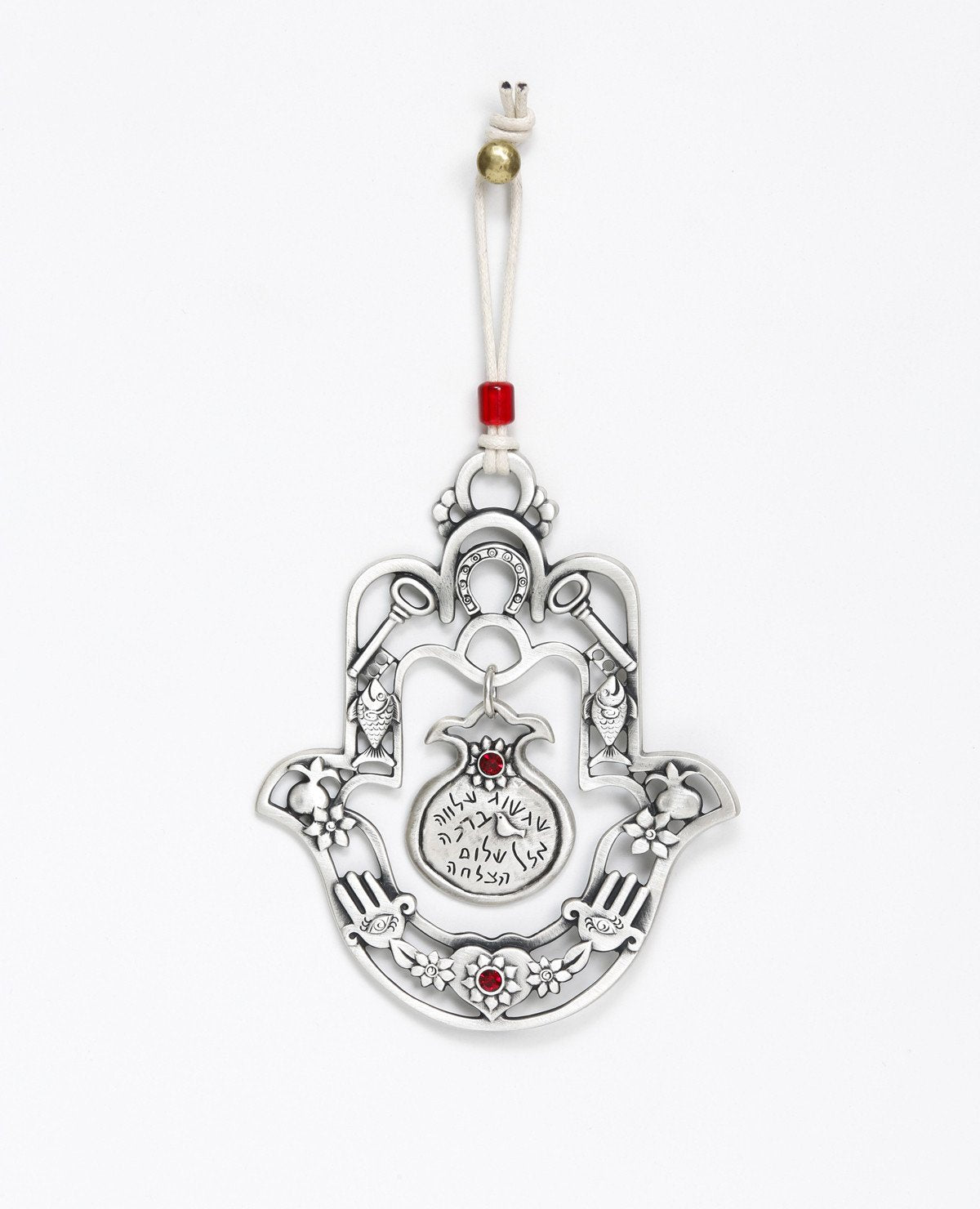A hanging Hamsa ornament with a delicate filigree like design and a hollow pomegranate hanging at its center. The Hamsa is decorated at its edges with pairs of motifs from the world of good luck charms and blessings, among them a pomegranate, a flower, a fish and a key. All these face each other to multiply the strength of the blessings. Words that bestow prosperity, serenity, blessings, peace and success are written on the pomegranate which hangs from the center of the Hamsa. The ornament is coated in ster