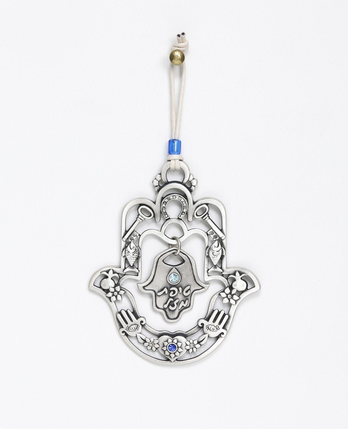 A hanging Hamsa ornament with a delicate filigree like design and a small Hamsa hanging from its center with the words "Drop of Luck". The Hamsa is decorated at its edges with pairs of motifs from the world of good luck charms and blessings, among them a pomegranate, a flower, a fish and a key. All these face each other to multiply the strength of the blessing. The ornament is coated in sterling silver and embedded with blue colored Swarovski crystals. Comes with a natural colored faux leather string, decor