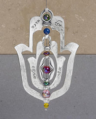 An impressive and neatly designed hanging Hamsa ornament coated in sterling silver. Set on an axis inside a large Hamsa is a smaller Hamsa. The axis is made from a thin string coated in silver and decorated by colorful beads. The ornament spins on the axis, and on each side appear different words of blessing. The qualities of the Hamsa on one side and the power of the words respectively on the other. A great gift that is also a joyful and heartwarming blessing, for any occasion. The ornament comes with a fa