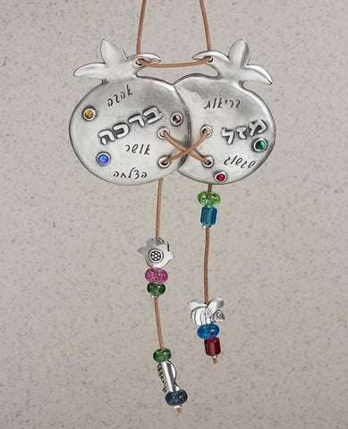 Two are better than one! A sweet and charming hanging ornament with a smile and a blessing. The pair of pomegranates are connected to each other, coated in sterling silver and embedded with colorful stones. A natural colored faux leather string is weaved between the pomegranates, with the ends dangling from the bottom of each, decorated by colorful beads and tiny heart and Hamsa decorations. The top part of the string serves for hanging the ornament. Engraved on the pomegranates are words of blessing: luck,