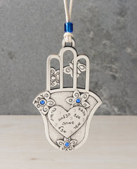 An aritistic, charming and delicately designed Hamsa hanging ornament. The Hamsa is coated in sterling silver and on its bottom part has a smooth plate with a big heart on it. Written inside the heart are seven blessings for: love, abundance, success, happiness, health, joy and luck. Surrounding the heart are flower decorations embedded with blue colored stones. On the top part of the Hamsa are three hollowed out fingers, with butterflies in between them. The ornament comes with a natural colored faux leath