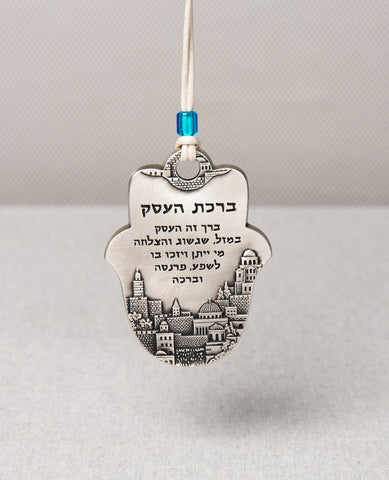 An impressive and excitingly designed hanging Hamsa Business Blessing. The Hamsa is coated in sterling silver and comes with a faux leather string  for hanging decorated by a blue bead. Engraved on the bottom part of the Hamsa an image of beautiful Jerusalem, and in the upper part appear blessing words of abundance, luck, prosperity, success and good fortune. The hanging ornament makes the perfect gift as a gesture of good intention for any business, old or new.   Length: 9 cm  Width: 6 cm