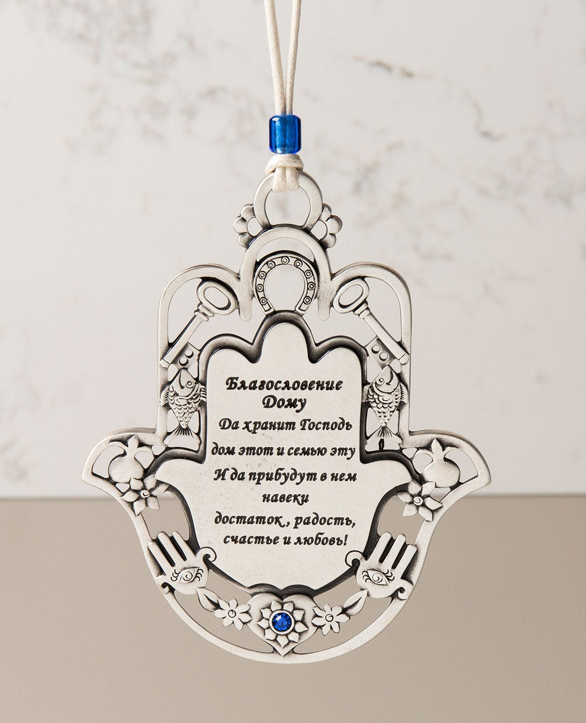 An impressive and exceptionally designed hanging Home Blessing. Shaped like a Hamsa and decorated by motifs such as a key, a fish, a horseshoe and a pomegranate, which according to Judaism symbolize respectively: a new way, fertility, luck and abundance. The ornament is coated in sterling silver, embedded with blue Swarovski crystals and comes with a faux leather string for hanging, decorated with a blue bead. A fantastic gift to grant any new home. Great for new beginnings, or for anyone you wish to greet 