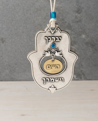 A designed hanging Hamsa ornament that carries on it the blessing of "May the Lord bless you and keep you safe", words that were added to the Kohen's blessing out of Jacob's blessing before his death to Joseph's sons - Ephraim and Manasseh. The Hamsa is coated in sterling silver combined with brass and has the blessed sentence embossed. Embedded at the center is a blue Swarovski stone and a pair of doves with an olive branch. At the top and bottom of the Hamsa are Stars of David. The Hamsa hangs from a natu