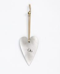 A "love makes a house a home" hanging ornament designed in the shape of a gracefully decorated heart and coated in sterling silver. Because what else turns walls and a roof into a home if not the love that dwells within them? Designed as an elongated heart shaped plate, on one side is the above sentence in English and a small embossed heart, and on the other is a pair of embossed loving hearts. The ornament comes with a natural colored faux leather string. Elegantly and cordially designed, it makes for a ch