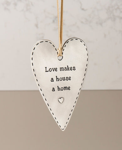 A "love makes a house a home" hanging ornament designed in the shape of a gracefully decorated heart and coated in sterling silver. Because what else turns walls and a roof into a home if not the love that dwells within them? Designed as an elongated heart shaped plate, on one side is the above sentence in English and a small embossed heart, and on the other is a pair of embossed loving hearts. The ornament comes with a natural colored faux leather string. Elegantly and cordially designed, it makes for a ch