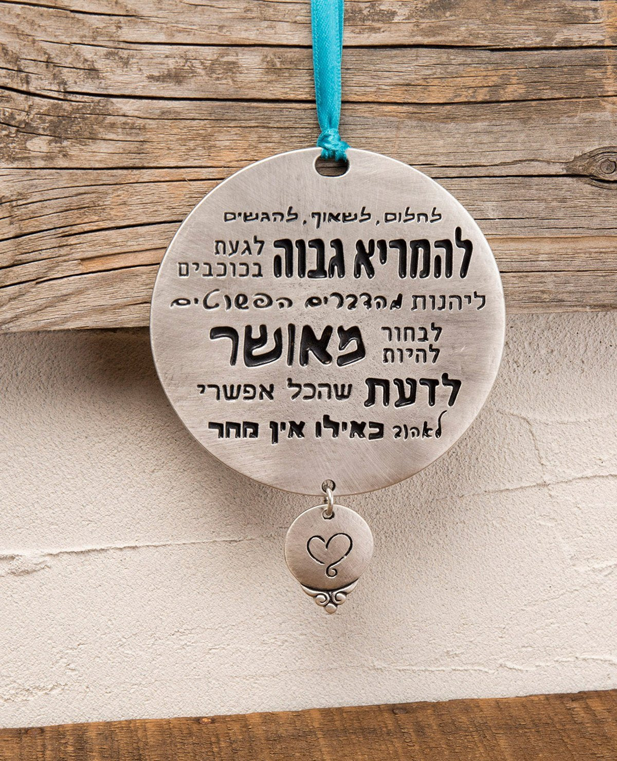A round hanging wall ornament that reminds us of the truly important things in life! The pendant is coated in sterling silver and has inspirational sentences engraved on it that remind us how it is best to live life: dream, aspire, and fulfill. Makes a great present that warmly embraces anyone you love, when you wish to cheer them up and make them happy, and when you wish to remind them of what is really important. The ornament comes on a turquoise colored ribbon for hanging.  Length: 12 cm  Width: 9 cm