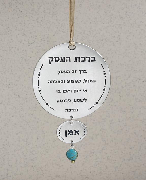 A hanging Business Blessing ornament in the form of two circles coated in sterling silver with a turquoise colored bead. The words of blessing praise the business with luck, prosperity and success. A joyful and thoughtful gift that blesses anyone who may receive it. Comes with a brightly colored satin string for hanging.  Length: 13.7 cm  Width: 9 cm