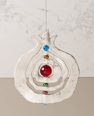 A pomegranate hanging ornament with a unique design that grants it motion which hypnotizes the eye with beauty. The pendant is designed in the shape of a hollow pomegranate with circular shapes at its center which are thread around one central axis, with colorful beads between them. The pendant is coated in sterling silver and hangs from a thin and strong silver string. Always suitable as a unique gift, embodying within it the pomegranate's blessing of abundance and fertility. Especially suitable around Ros