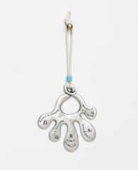 An open hand Hamsa wall ornament that hangs from a natural colored faux leather string decorated by a turquoise colored bead. The Hamsa is coated in sterling silver and each finger has a blessing engraved on it in English and Chinese. The blessings are from the world of Feng Shui, the ancient Chinese philosophy which represents the way of peace and harmony. Luck, abundance, harmony, peace, longevity, joy and more joy, these are the loving blessings which you can grant to whoever will receive this charming g