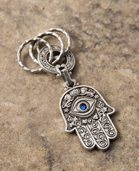 A double sided Hamsa keychain coated in sterling silver. On one side is a big eye embedded with a blue colored Swarovski crystal and embossed lions. On the other side are embossed birds, pomegranates, fish and grapes. The whole Hamsa is decorated in a filigree like style. The connecting links and the key rings are massive and strong. It's fun to connect our most important keys to it and most definitely to grant our loved ones with such a beautiful Hamsa, blessed with the many icons of good fortune, protecti