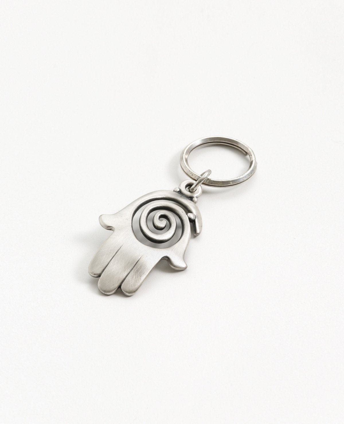 A charming and uniquely designed Hamsa shaped keychain which incorporates a full design with the empty spaces within the spiral. The Hamsa is coated in sterling silver and is slightly concave. It is so beautiful that you can just keep staring at it over and over, feel its different textures and sense the blessing within. A strong and reliable keychain that makes a great gift for your loved ones.  Length: 7 cm  Width: 4 cm