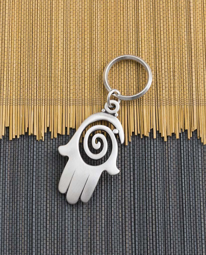 A charming and uniquely designed Hamsa shaped keychain which incorporates a full design with the empty spaces within the spiral. The Hamsa is coated in sterling silver and is slightly concave. It is so beautiful that you can just keep staring at it over and over, feel its different textures and sense the blessing within. A strong and reliable keychain that makes a great gift for your loved ones.  Length: 7 cm  Width: 4 cm
