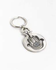 A blessing every time you open and lock. A charming keychain coated in sterling silver and carrying a blessing that follows you wherever you go. A Hamsa hangs within the hollow pomegranate frame. On it's one side an eye embedded with a blue colored crystal and a charm against the "evil eye", and on the other side appear the words "Hamsa On You" decorated with flowers, for luck and blessing. All of these are contained within the pomegranate, which brings the blessings of abundance and fertility. A suitable a