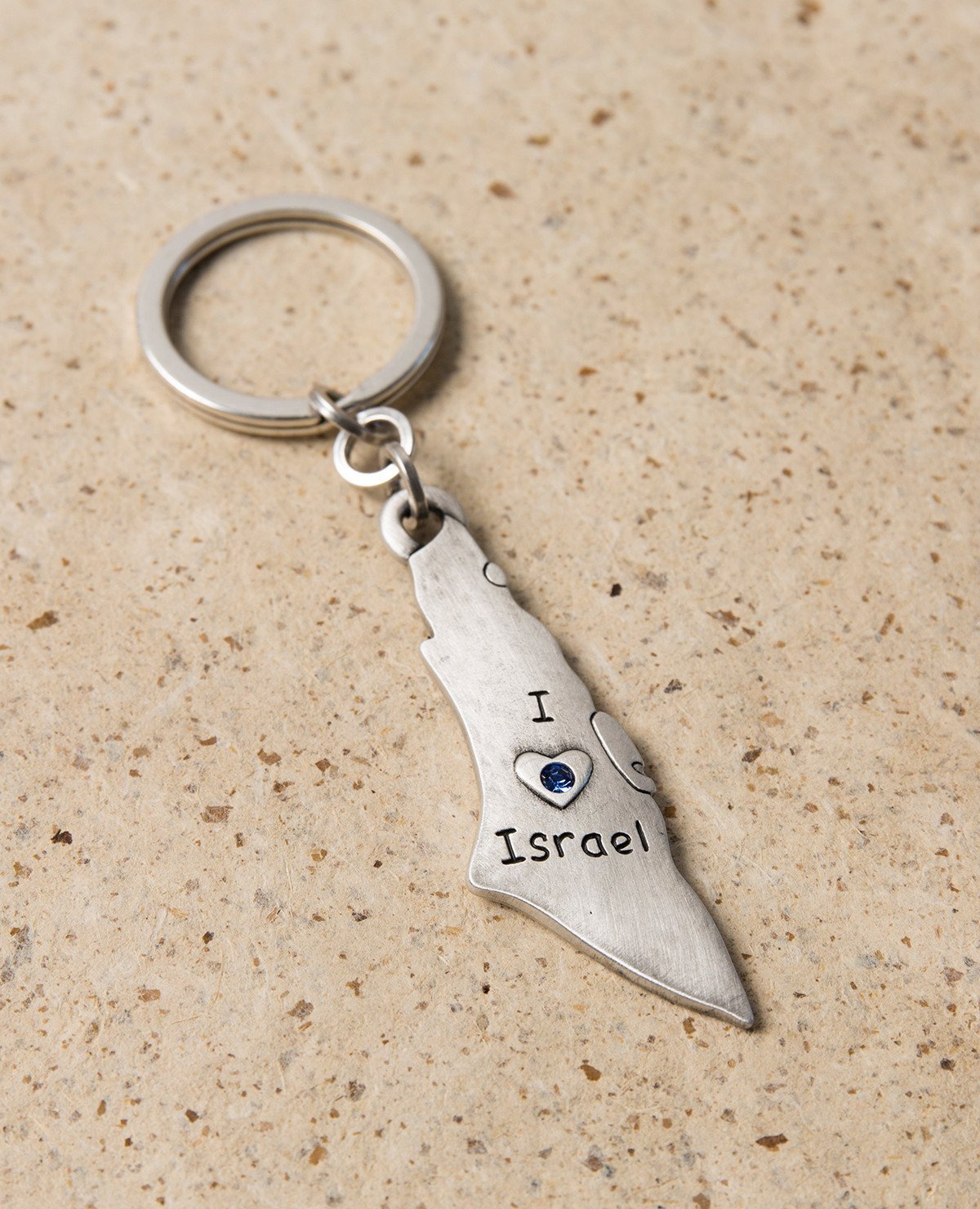 A charming keychain for Israel lovers, in English and designed in the shape of a map of Israel. Engraved on one side are the words "I Love Israel" with a heart embedded with blue colored Swarovski crystals, and on the other side a flag of Israel. The keychain is coated in sterling silver and is strong and reliable. This reminder of the simple love for Israel makes a great gift for friends and family in Israel and abroad.   Length: 7 cm  Width: 2 cm