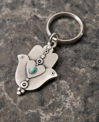 An extraordinarily beautiful keychain with a rare design, coated in sterling silver. On one side of the Hamsa is a dove inlaid with a turquoise colored Swarovski crystal. Engraved on top is the Kohen's blessing "May the Lord bless you and keep you safe". On the other side of the Hamsa are two doves looking in opposite directions, with a heart in between them that is also embedded with a turquoise stone. A keychain that is all beauty and blessings. The Hamsa's blessing for good luck, the doves blessing for p