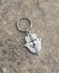 A extraordinarily beautiful keychain with a rare design, coated in sterling silver. On one side of the Hamsa is a dove inlaid with a blue colored Swarovski crystal. Engraved on top is the Kohen's blessing "May the Lord bless you and keep you safe". On the other side of the Hamsa are two doves looking in opposite directions, with a heart in between them that is also embedded with a blue stone. A keychain that is all beauty and blessings. The Hamsa's blessing for good luck, the doves blessing for peace and lo
