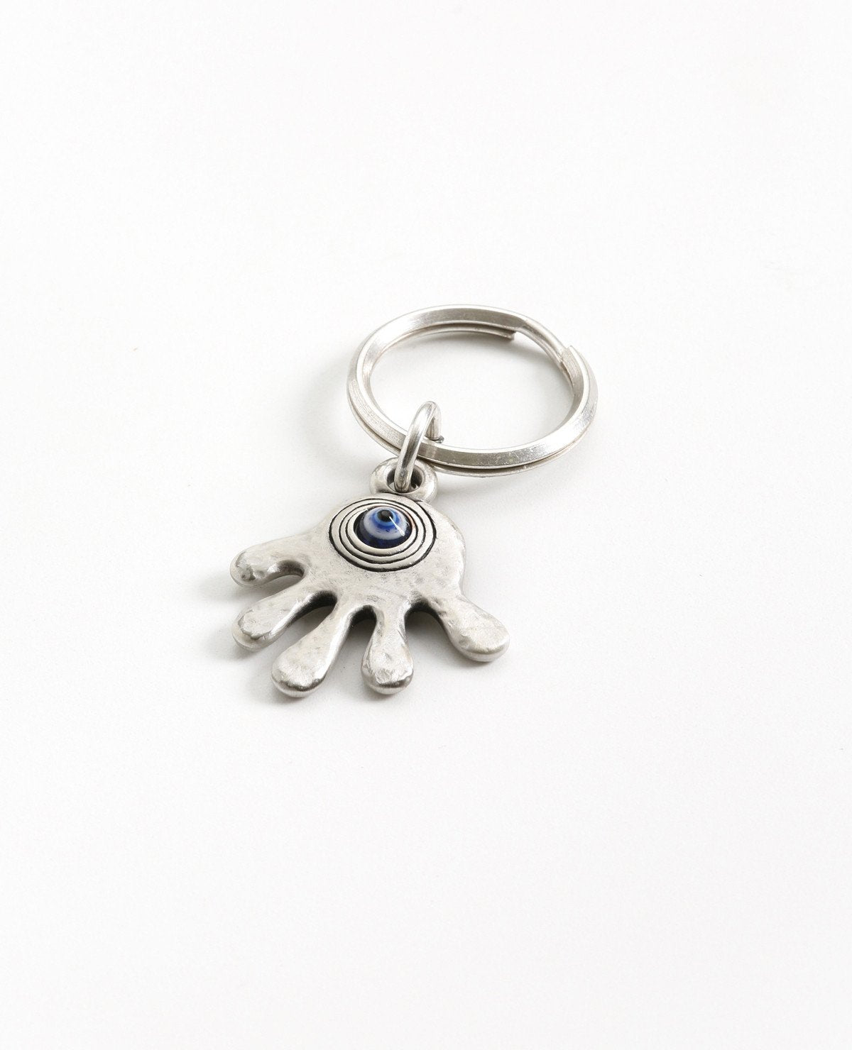 A fun and optimistic keychain that faces forward. Coated in sterling silver and designed in the shape of a Hamsa with fingers spread. On one side a decorated blue eye, and the other side is engraved with the words "every ending is a new beginning". A wonderful gift for all the endings or beginnings in life. The possibilities are endless, the protection is already inside, or how shall we put it gently.... Hamsa Hamsa!  Length: 5 cm  Width: 4 cm