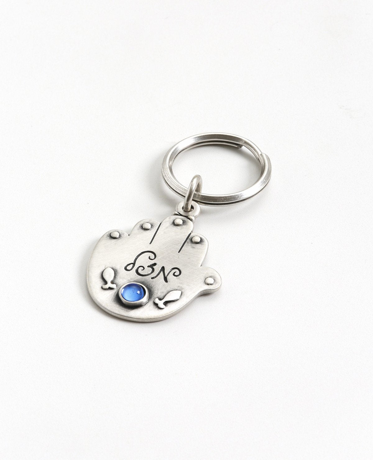 An exciting double-sided Hamsa keychain. On one side of the Hamsa the words "Good journey and safe travels!" are written. Written on the other side is the word "Luck" with a blue stone embedded underneath, and next to it an embossed image of two fish.
The Hamsa is coated in sterling silver and is strong and reliable to accompany your loved ones throughout the entire journey. A charming and loving gift for anyone about to embark on a trip in the voyage of life. A present that will leave our loved ones with a