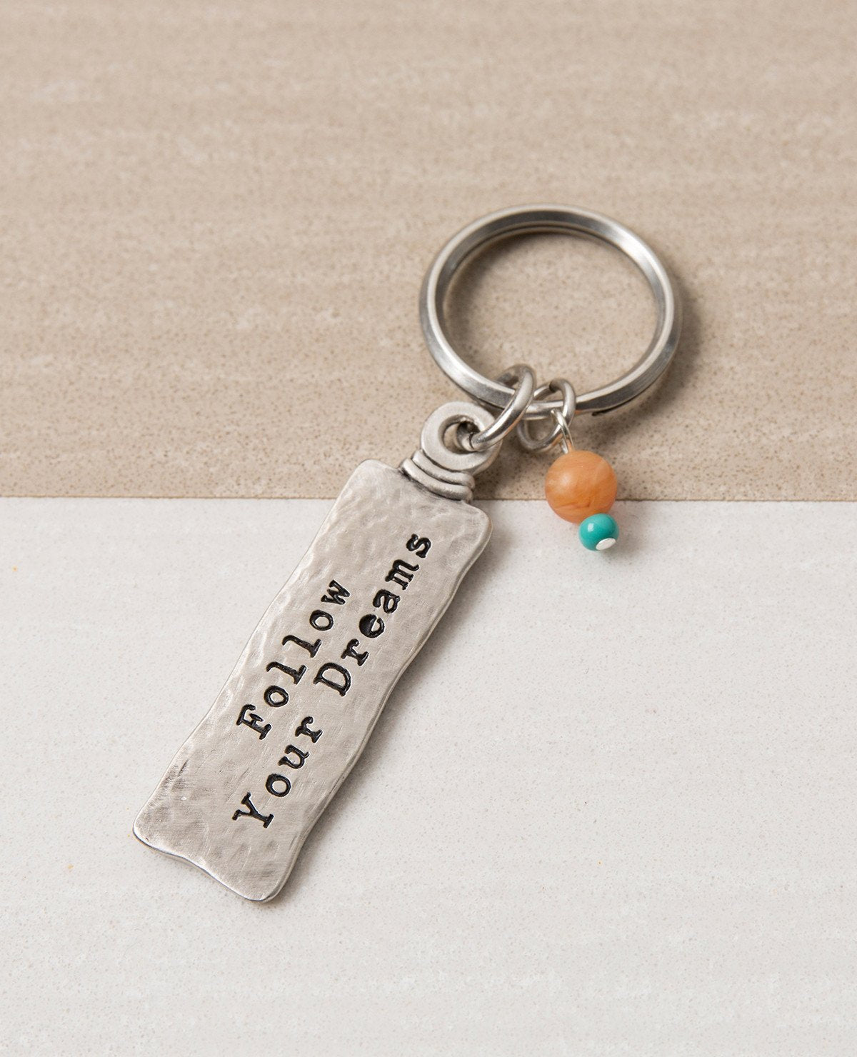 The gift that is most fun to give! A classically designed keychain - for him or for her. Shaped like an elongated rectangle with the words "Follow Your Dreams" on one side and embossed leaves decorating the other side. At the top of the keychain are two differently colored beads in the charming mix of orange and turquoise. The keychain is coated in sterling silver and is strong and reliable. A great gift to give to someone you love, anyone beginning a journey, or simply as a reminder that most important is 