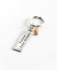 The gift that is most fun to give! A classically designed keychain - for him or for her. Shaped like an elongated rectangle with the words "Follow Your Dreams" on one side and embossed leaves decorating the other side. At the top of the keychain are two differently colored beads in the charming mix of orange and turquoise. The keychain is coated in sterling silver and is strong and reliable. A great gift to give to someone you love, anyone beginning a journey, or simply as a reminder that most important is 
