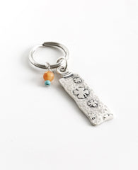 The gift that is most fun to give! A classically designed keychain - for him or for her. Shaped like an elongated rectangle with the words "Follow Your Dreams" on one side and embossed leaves decorating the other side. At the top of the keychain are two differently colored beads in the charming mix of orange and turquoise. The keychain is coated in sterling silver and is strong and reliable. A great gift to give to someone you love, anyone beginning a journey, or simply as a reminder that most important is 