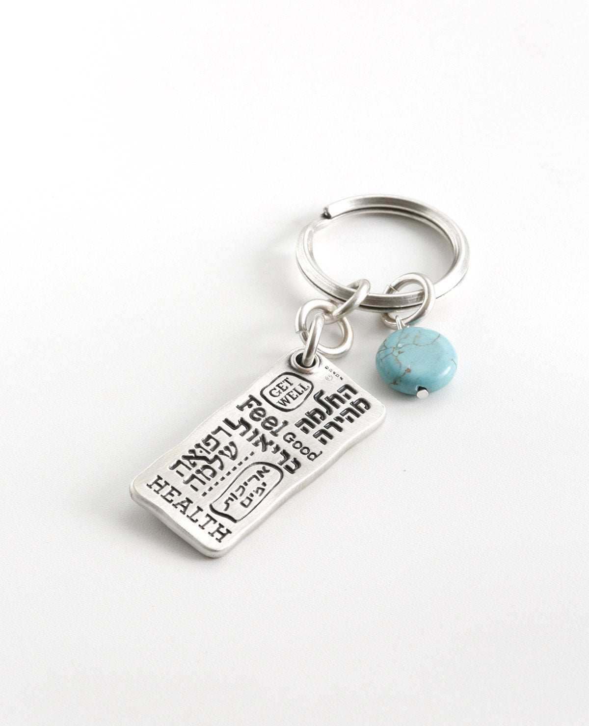 A beautiful and excitingly designed keychain, the content of which was taken from a prayer by Moses for the health of his sister, and it is in fact a prayer for good health. Shaped as a rectangular plate that has the sentence "Please, God, heal her" written in Hebrew on one side, and underneath an embossed image of a Hamsa with an eye. The other side contains blessings, in both English and Hebrew, for quick recovery, good health, and longevity. Next to the plate hangs a pretty turquoise stone. The keychain 
