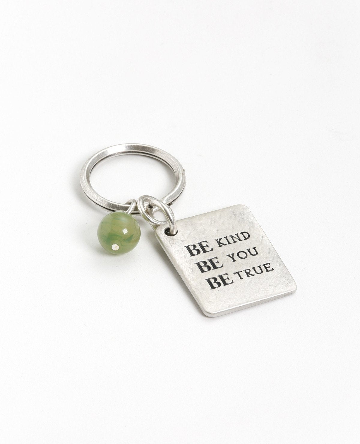 A keychain that is all charm, beauty and carries a very human message. Designed as a rectangular plate with the words "Be Kind Be You Be True" written in English on one side. The other side has an embossed image of a wide treetop and roots. Next to the plate hangs a stunningly beautiful green stone. The keychain is coated in sterling silver and is strong and reliable. A great gift for him or for her, here or anywhere, with the deepest and simplest message: be generous, be who you are, be real. This signific