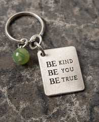 A keychain that is all charm, beauty and carries a very human message. Designed as a rectangular plate with the words "Be Kind Be You Be True" written in English on one side. The other side has an embossed image of a wide treetop and roots. Next to the plate hangs a stunningly beautiful green stone. The keychain is coated in sterling silver and is strong and reliable. A great gift for him or for her, here or anywhere, with the deepest and simplest message: be generous, be who you are, be real. This signific