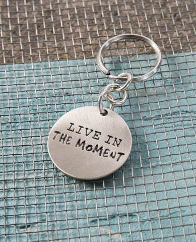 A keychain with an inspiring message: live the moment! What has happened is history, and what will be is a mystery. So all that is left is to experience the moment in its entirety. The keychain is designed as a round hanger with the words "Live In The Moment" written on one side, and on the other an embossed image of a large bird coated in copper, with black birds flying around it. All this on a backdrop coated in sterling silver. The keychain is strong and reliable. Makes a great gift with a message for He