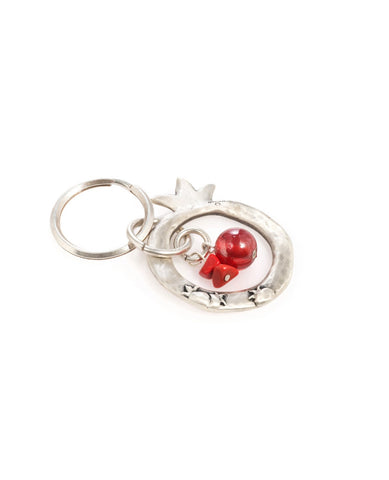 A charming keychain with an important message for life. The keychain is designed as a hollow pomegranate coated in sterling silver. At its center hang a red bead and two beautiful red stones. Written on one side of the pomegranate frame are the words "Let go of the past, embrace the present, dream the future". On the other side of the frame are little pomegranate decorations. The keychain is strong and reliable. A wonderful and exciting gift for him or for her, or for anyone in fact who wants to live life a