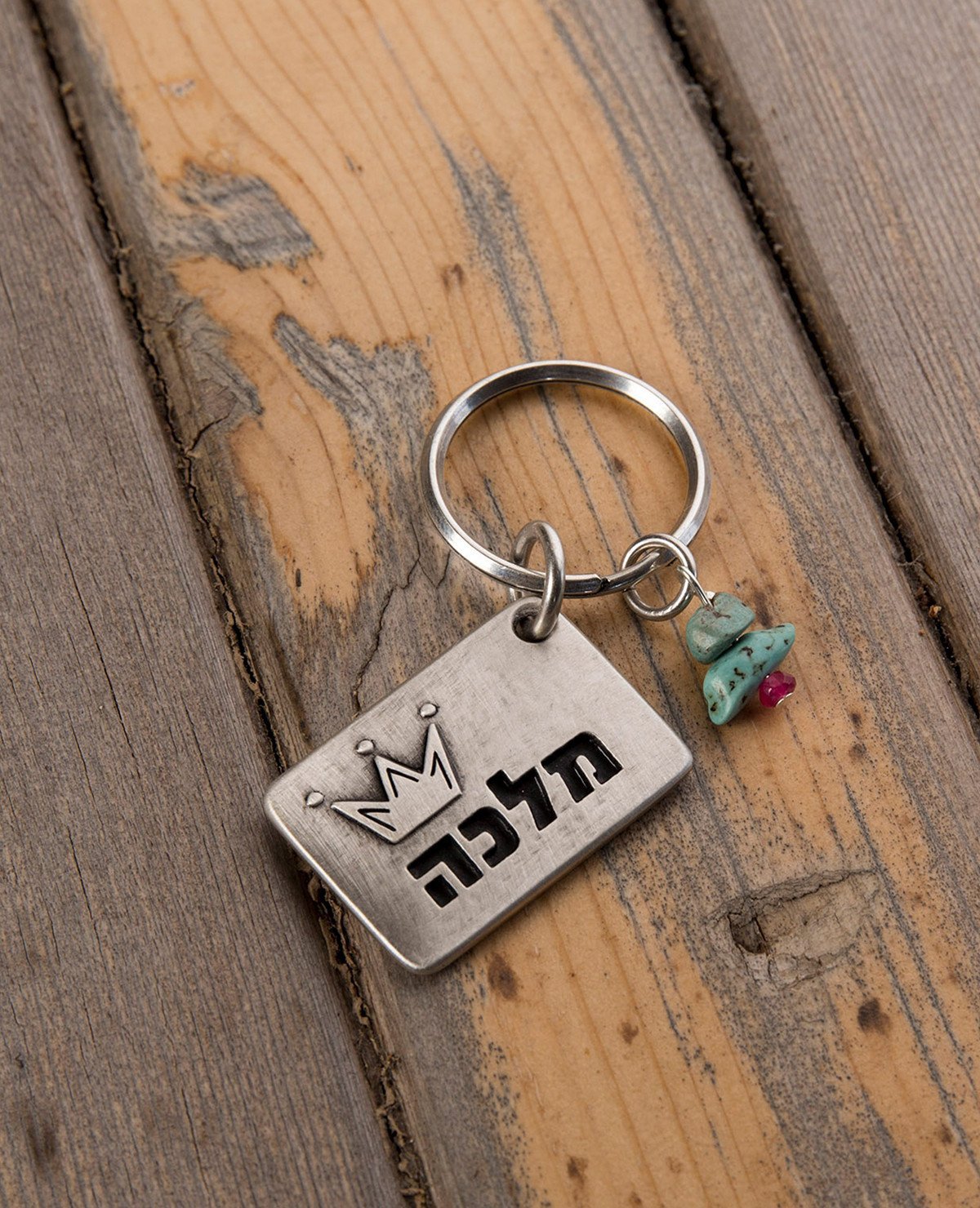 A majestic and meaningful keychain, intended specifically for your queen. Designed as a rectangle coated in sterling silver, with the word "Queen" written on one side, along with an embossed crown. On the other side is an embossed crown. Next to the rectangle hang three colorful beads. The keychain is strong and reliable. Makes a great gift that says it all, for the queen who is only yours.   Length: 3 cm  Width: 4 cm