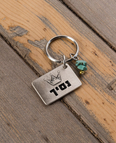 A simple and charming keychain, intended specifically for your prince. Designed as a rectangle coated in sterling silver with the word "Prince" written on one side, along with an embossed crown. On the other side is an embossed crown. Next to the rectangle hang two turquoise colored beads and a gold colored bead. The keychain is strong and reliable. Makes a great gift to embrace all the princes in your kingdom with a hug.   Length: 3 cm  Width: 4 cm